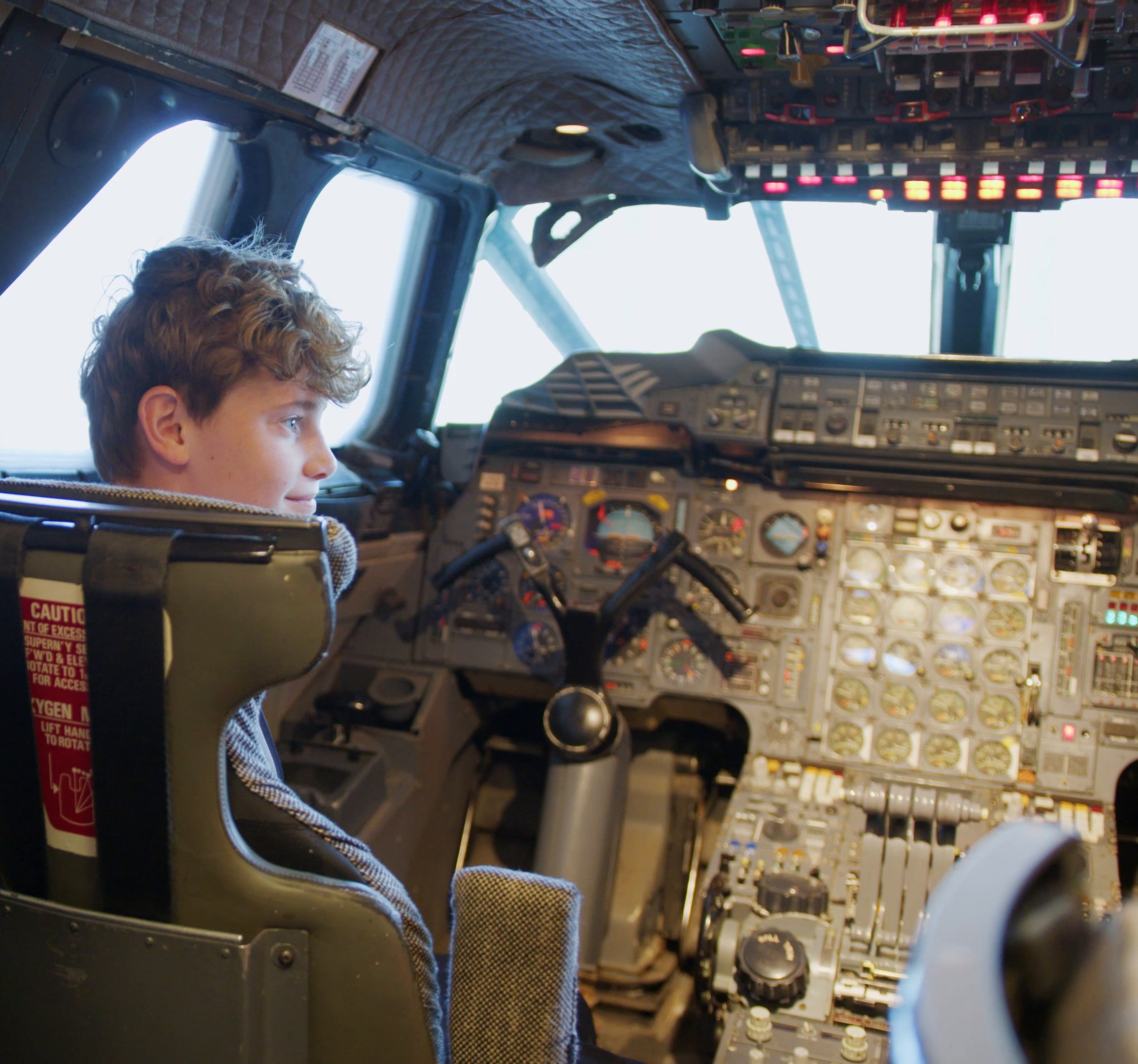 A teenager sitting in the pilot's seat on Concorde's flight deck, looking out of the window.